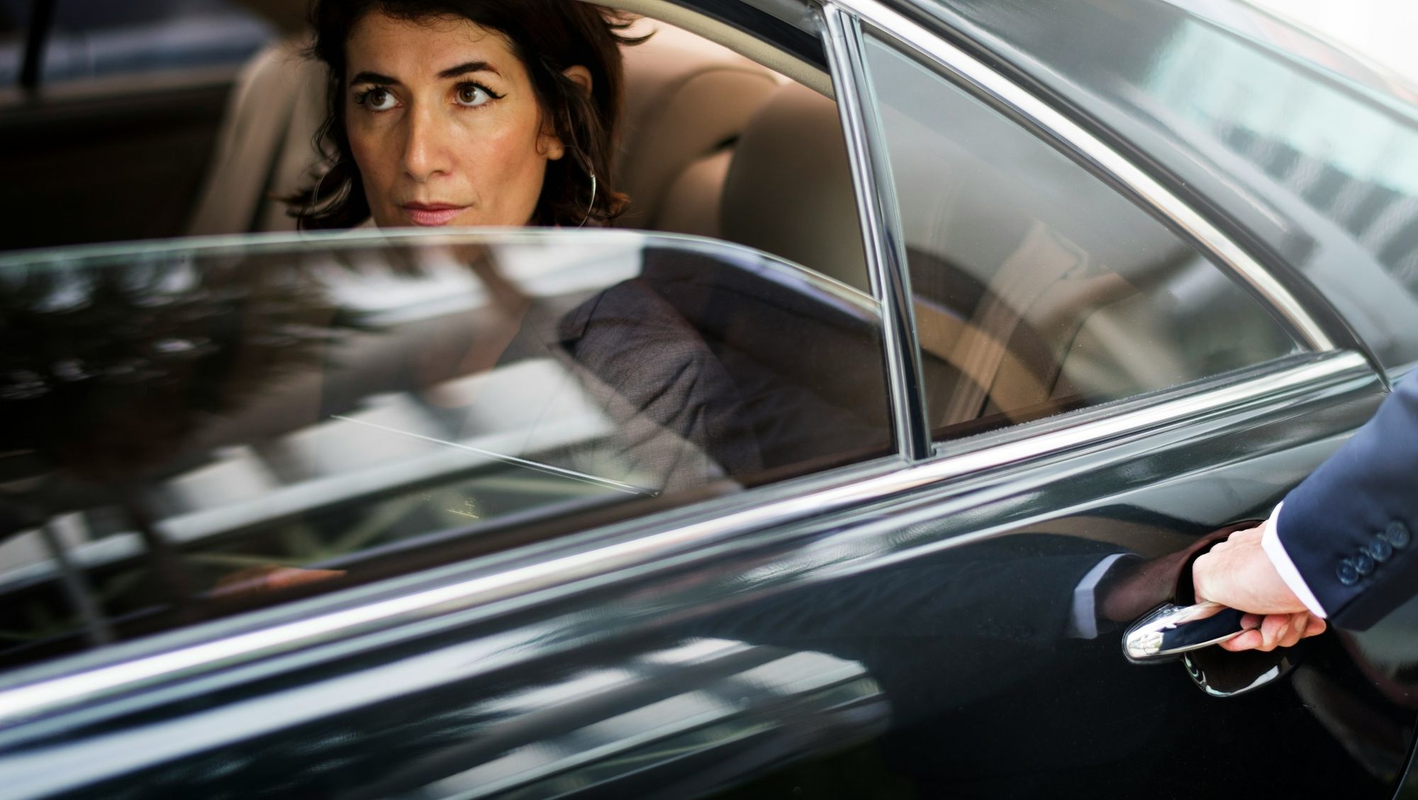 Passenger in the back of a black Mercedes as a chauffeur opens the door